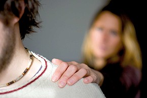 Frau verschwommen im Hintergrund legt Hand auf die Schulter eines Jugendlichen