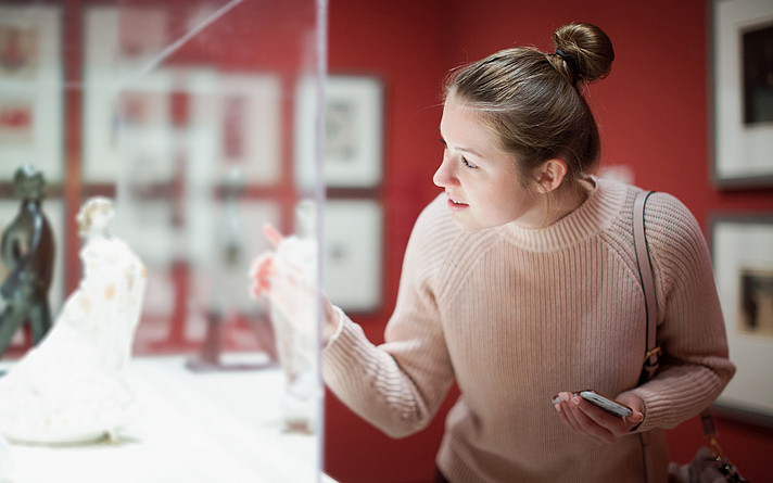 Young woman visitor using  phone  in museum