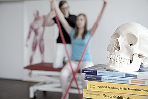 Schädel eines Menschen auf Büchern, im Hintergrund physiotherapeutische Übung